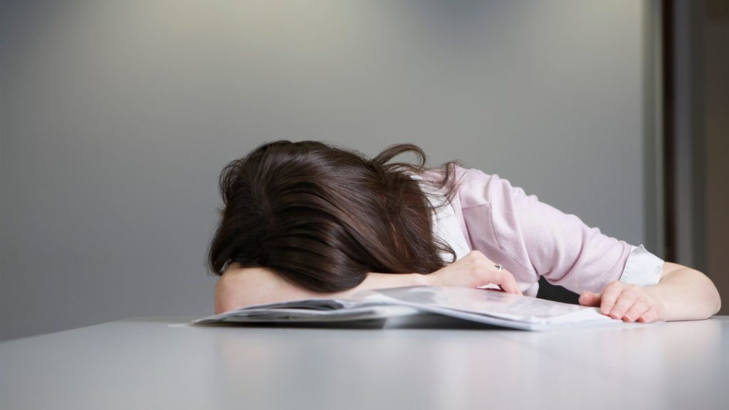 donna stanca accasciata su un libro, a simboleggiare la Stanchezza e il suo effetto su chi soffre di malattie neuromuscolari